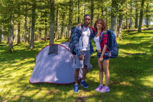 Young hikers posing together next to their tent in a beautiful sunny forest, enjoying the tranquility of nature during their camping adventure