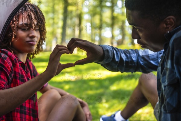 Happy couple making heart shape with hands while camping in nature, enjoying a romantic moment together
