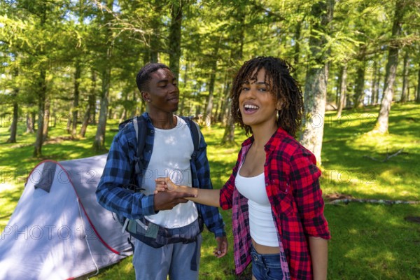 Happy smiling backpackers holding hands near tent in the woods, enjoying summer vacation camping trip