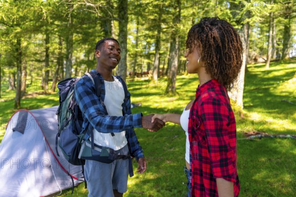 Two hikers shaking hands near tent in forest, enjoying camping trip and celebrating teamwork and partnership