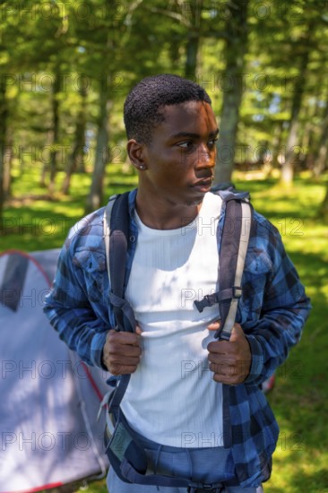 Young hiker wearing backpack exploring forest near campsite, enjoying outdoor adventure and embracing the tranquility of nature