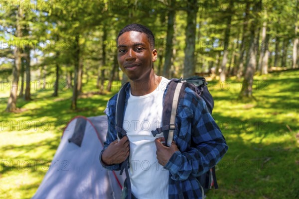 Young black man wearing a backpack, enjoying a camping trip in the woods, surrounded by lush trees and the beauty of nature