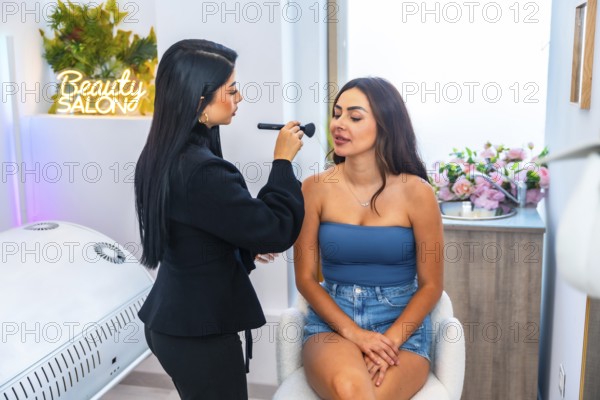 Beautician applying makeup with a brush on a young woman's face in a vibrant beauty salon, enhancing her natural beauty and confidence