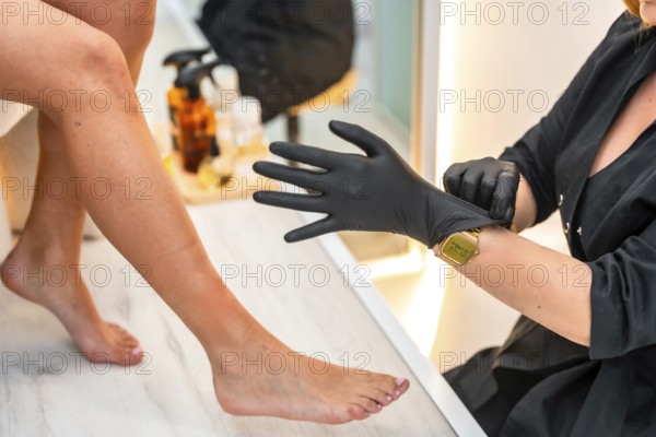 Beautician putting on black gloves, preparing for a beauty treatment on a client's legs in a beauty salon