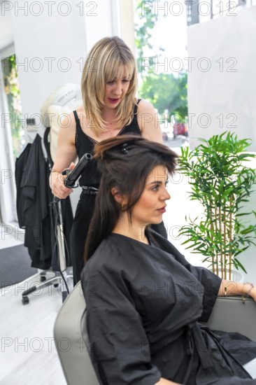 Hairdresser styling client's hair with curling iron in modern beauty salon, creating fashionable hairstyle