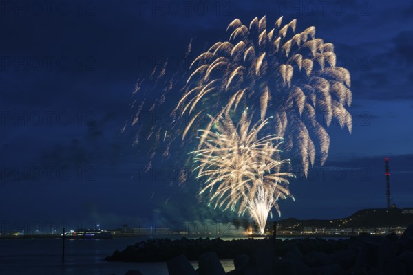 Radiant luminous colours, atmospheric fireworks in green and gold, Heligoland island festival, Unterland with inland harbour, jetty and lobster shacks, on the right the Oberland with transmission tower, transmitter, night shot, in front the groyne of the dune, reflecting water of the North Sea, Night sky at the island festival, summer, symbolic image also for New Year's Eve, New Year's Eve fireworks, luminous, colourful, impressive atmosphere, traces of light, lively glitter, night, Heligoland Island, Schleswig-Holstein, Germany