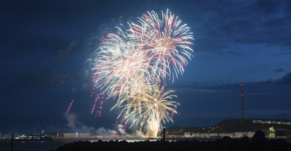 Bright illuminated colours, atmospheric fireworks in red, green and gold, Heligoland island festival, Unterland with inland harbour, jetty and lobster shacks, on the right the Oberland with transmission tower, transmitter, night shot, in front the groyne of the dune, reflecting water of the North Sea, night sky at the island festival, summer, symbolic image also for New Year's Eve, New Year's Eve fireworks, bright, colourful, festive, colourful traces of light, lively glitter, night, Heligoland Island, Schleswig-Holstein, Germany