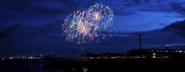 Radiant luminous colours, atmospheric fireworks in red, green and gold, Heligoland island festival, Unterland with inland harbour, jetty and lobster shacks, on the right the Oberland with transmission tower, transmitter and lighthouse, night shot, in front the groynes of the dune, reflecting water of the North Sea, night sky at the island festival, summer, symbolic picture also for New Year's Eve, New Year's Eve fireworks, bright, colourful, colourful traces of light, lively glitter, night, Heligoland Island, Schleswig-Holstein, Germany