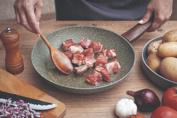 Diced pork meat, with vegetables, on a wooden kitchen table, in a cozy home environment