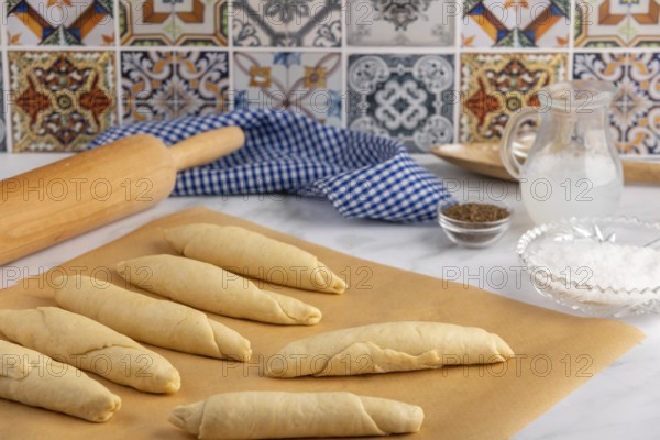 Rolled, raw pretzel sticks on baking paper with rolling pin and spices