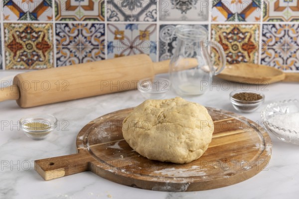 Dough on a wooden board with rolling pin and bowls in front of colourful tiles