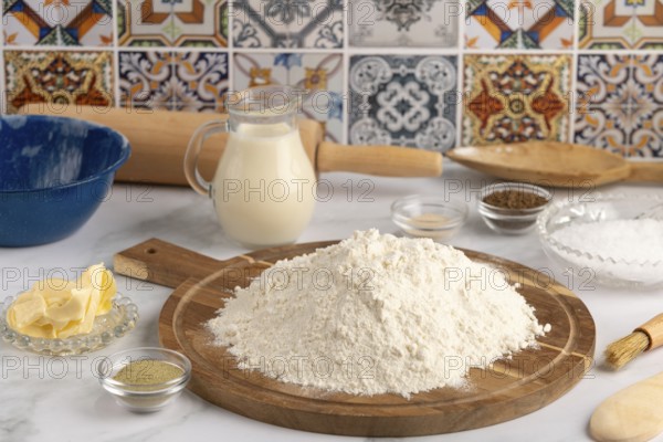 Pile of flour on a wooden board surrounded by various baking ingredients in a kitchen