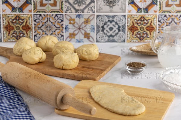 Dough balls on a wooden board with a rolled out dough, rolling pin next to it