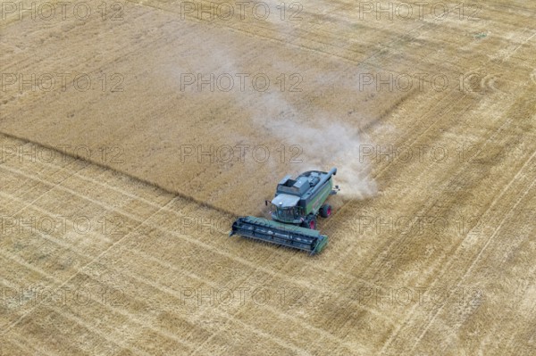 A combine harvester harvests a grain-covered field and stirs up dust, basket in the Rems Valley, Baden-Württemberg, Germany
