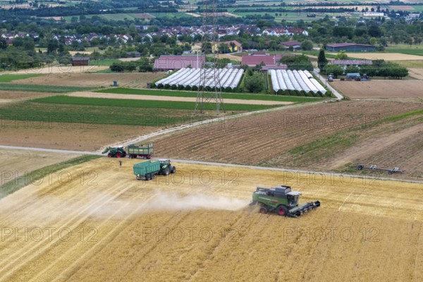 A combine harvester and tractor operate in a field in a rural area near a village