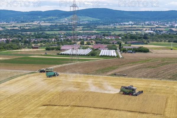 Wide fields with combine harvesters and tractors against a backdrop of mountains and a power pole, Korb im Rems Valley, Baden-Württemberg, Germany
