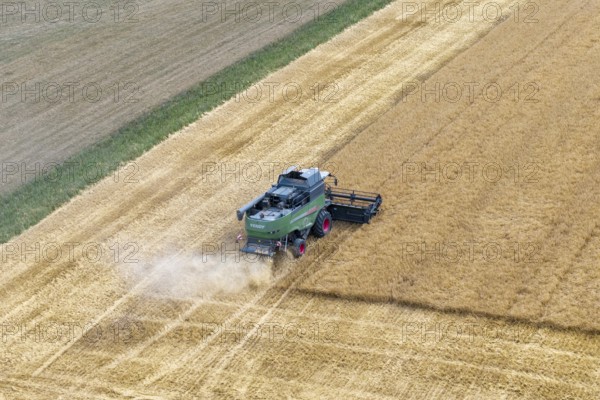 A combine harvester harvests a cornfield and moves through the dusty landscape, Korb im Rems Valley, Baden-Württemberg, Germany