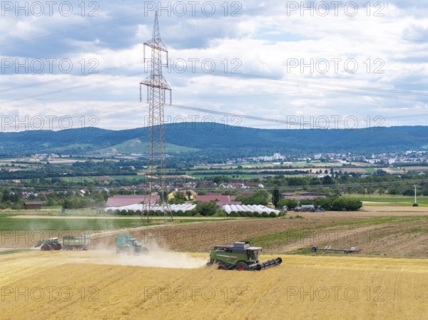 A combine harvester works near a power pole in a vast rural landscape under cloudy skies, Traktore Korb im Remstal, Baden-Württemberg, Germany