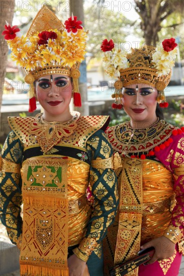 Legong dancers in traditional costumes, wearing makeup, in front of a dance performance in Sanuar, Bali Indonesia