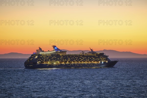 Mykonos, Cyclades, Greece - Voyager of the Seas cruise ship sails from Mykonos harbour bay towards the evening sun at dusk