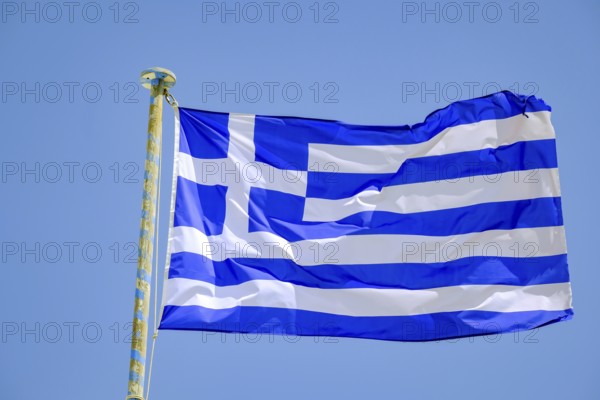 Ano Mera, Mykonos, Cyclades, Greece - Greek national flag fluttering on the flag pole on the roof of Panagia Tourliana monastery forms the center of Ano Mera. The men's convent from the 16th century on the village square in the interior of the island is now a tourist attraction much visited by tourists