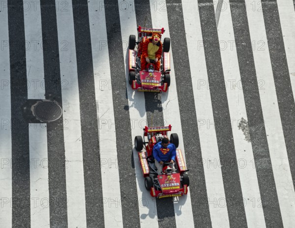 People in costumes drive small go-kart racing cars across zebra crossings, Shibuya Crossing, Shibuya, Tokyo