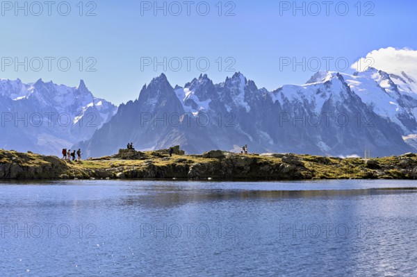 A group of hikers at Lac de Chésserys, behind the snow-covered Mont Blanc massif, Chamonix-Mont-Blanc, Haute-Savoie, France