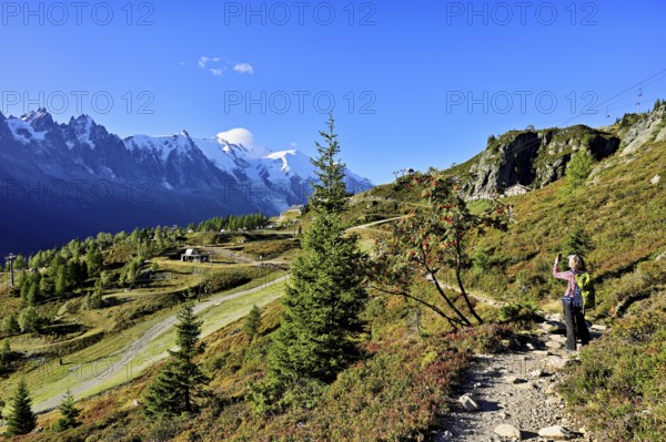 Female hiker on a hiking trail with the La Flégère cable car mountain station and the snow-covered Mont Blanc massif, Chamonix-Mont-Blanc, Haute-Savoie, France