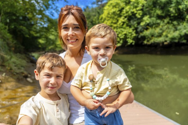 Mother and her two sons enjoying a sunny day by the river, capturing a joyful selfie while smiling together, creating lasting memories of family fun and togetherness