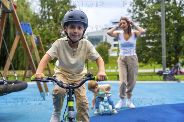 Happy children enjoying riding bicycles in a modern playground while their mother watches over them, promoting childhood activities, family bonding, and outdoor fun