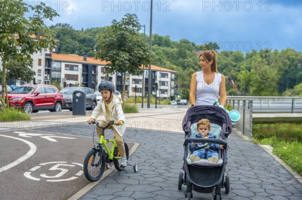 Mother pushing a baby stroller while her son rides a bicycle on a bike path in a modern urban environment, promoting healthy lifestyle and family bonding