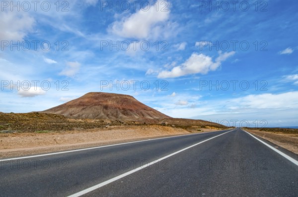 View of long straight paved road to the left partly eroded volcano volcanic cone in volcanic landscape volcanic landscape, Fuerteventura, Canary Islands, Spain