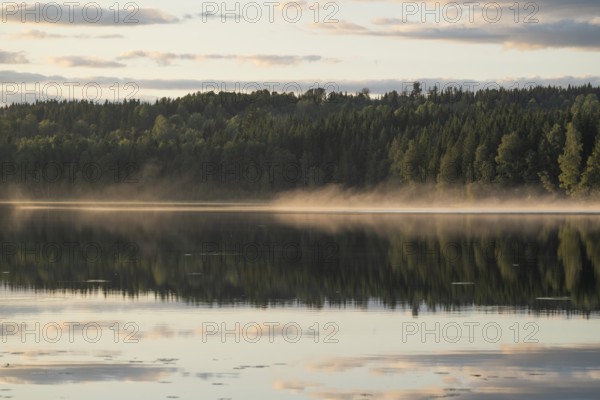 Rising fog, clouds reflected on the water surface, forest lake, evening mood, at Sunne, Sweden
