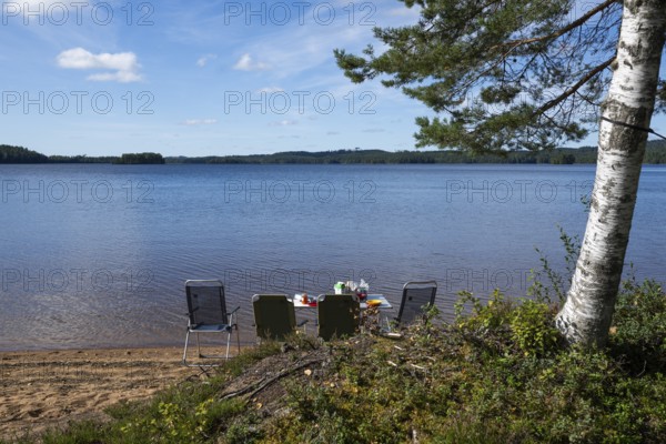 Camping chairs and camping table stand on lakeside, lake, surrounded by forest, near Sunne, Sweden