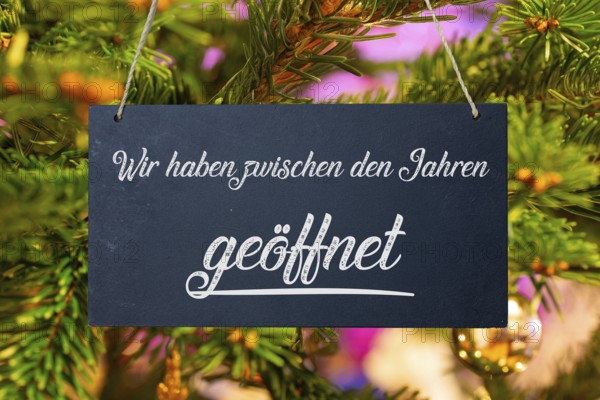 (photo montage) Christmas opening times: sign with the inscription WE ARE OPEN BETWEEN THE YEARS in front of a Christmas tree