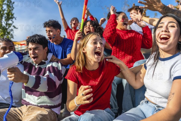 Diverse group of young adult sports fans cheering and shouting with arms raised in stadium stands, celebrating their team with energy, unity and weekend game excitement