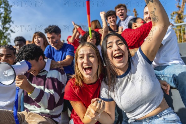 Group of excited young people watching a sports game and cheering with hands up and megaphones, creating a vibrant atmosphere of support and celebration