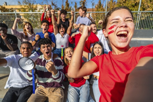 Diverse group of young adult fans energetically cheering and celebrating a win at a sports event, showing excitement, team spirit, and togetherness while watching from stadium bleachers