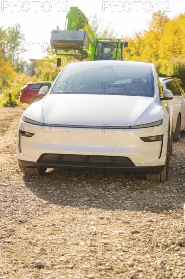 White electric car on a gravel path in autumn, surrounded by colorful foliage and trees, Telsa Model Y Juniper electric car, Gechingen, Germany