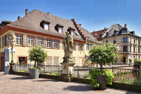 Ettlingen, Germany - August 13th 2025: Statue of Saint John of Nepomuk on Rathausbrücke bridge over River Alb with buildings in old town