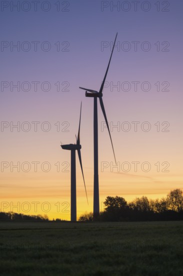 Two wind turbines rise at dusk. The sky shows a soft color gradient, in keeping with the peaceful surroundings, Swabian Jura, Baden-Württemberg, Germany