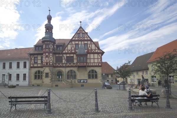 Historic town hall built in 1639, couple sitting on park bench, market square, half-timbered house, Harzgerode, Harz, Saxony-Anhalt, Germany