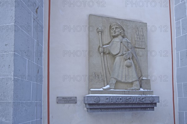 Memorial with pilgrim sculpture and stick on the Camino de Santiago de Compostela via Mayen to Santiago de Compostela, pilgrim trail, hiker, trekking, figure, stone, symbol, scallop, inscription, St. Clemens, Mayen, Vulkaneifel, Eifel, Rhineland-Palatinate, Germany