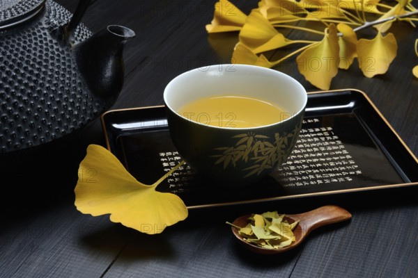 Ginkgo tea in tea bowl and ginkgo leaf, tea leaves in a spoon, ginkgo biloba