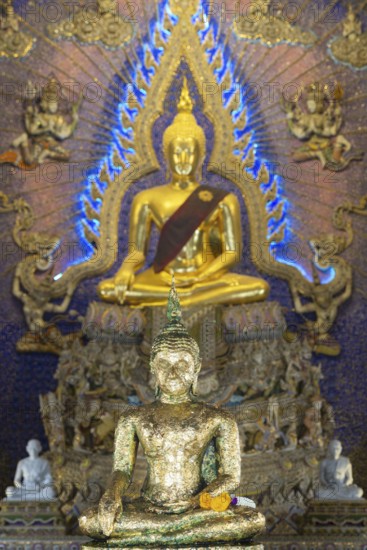 Buddha statue decorated with gold leaf, Bhumispara mudra, Buddha Gautama at the moment of enlightenment, behind another golden Buddha statue with tunic, art hall with modern art trends such as minimalism and abstraction, Wat Pariwat, Yan Nawa district, Bangkok, Thailand