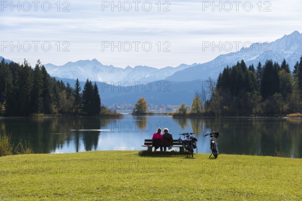 Two woman on a bench at Lake Forggensee enjoy the view of the mountains and the autumn landscape, bicycles are standing by Roßhaupten, Ostallgäu, Allgäu, Bavaria, Germany