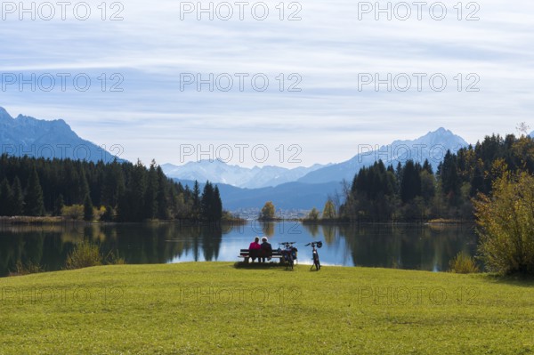Two woman sitting on a bench at Lake Forggensee with a view of mountains, surrounded by autumn trees and bicycles, near Roßhaupten, Ostallgäu, Allgäu, Bavaria, Germany