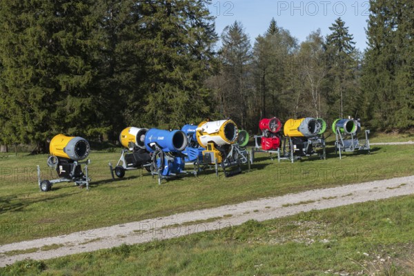 Row of snow cannons in a meadow in front of trees and blue sky, Schwangau near Füssen, Ostallgäu, Allgäu, Bavaria, Germany