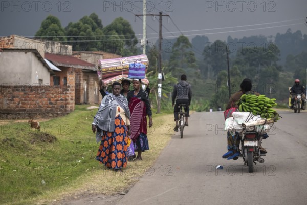 Street scene in rural Uganda, woman carrying bags and mattresses on their heads, motorcyclists loaded with bananas, Kisoro, Uganda