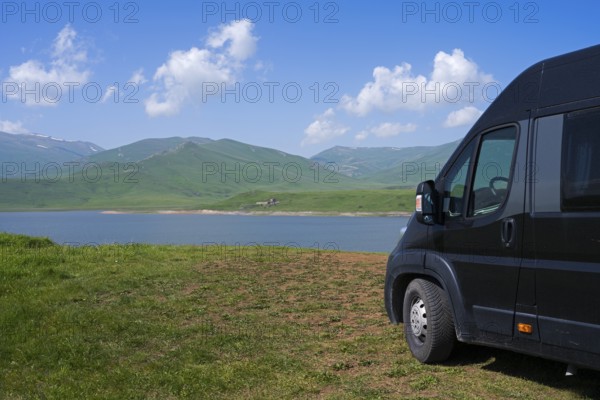 A black van stands at a lake with mountains in the background under a blue sky with clouds, camper, motorhome, Spandaryan Reservoir, Spandarian, fed by the Vorotan River, Vorotan, Syunik Province, Armenia